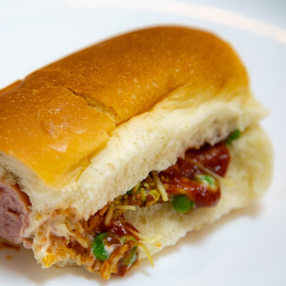 A Fitchy's Hoagy sandwich, filled with sausage, cheese, and various sauces, on a white plate.