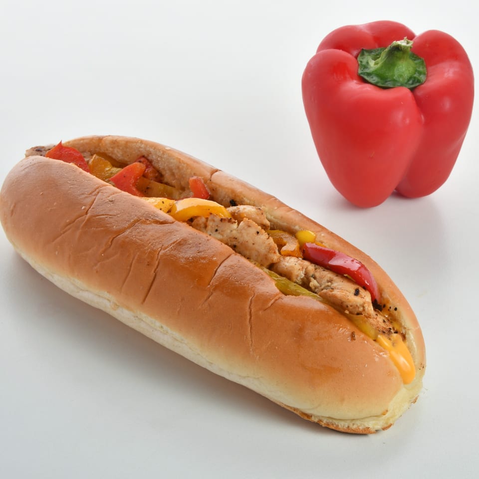 Fitchy's chicken hoagy with melted cheese, red and yellow peppers, next to a whole red bell pepper.